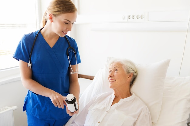 koncepcja medycyny, wieku, opieki zdrowotnej i ludzi - lekarz lub pielęgniarka pokazujący medycynę starszej kobiecie na oddziale szpitalnym