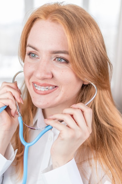 Koncepcja medyczna Uśmiechnięta pielęgniarka z szelkami i stetoskopem w dłoni Szczęśliwa i roześmiana lekarka w białym fartuchu pozująca przed kamerą Pracownik szpitala