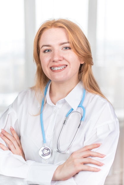 Koncepcja medyczna Uśmiechnięta pielęgniarka z szelkami i stetoskopem w dłoni Szczęśliwa i roześmiana lekarka w białym fartuchu pozująca przed kamerą Pracownik szpitala
