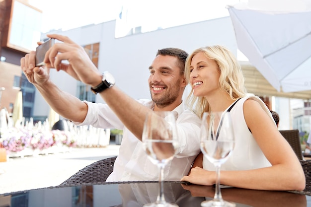 koncepcja miłości, daty, technologii, ludzi i relacji - uśmiechnięta szczęśliwa para robiąca selfie ze smartfonem na tarasie restauracji