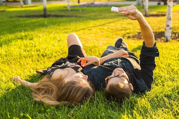 Koncepcja miłości i ludzi. szczęśliwa para nastolatków, leżąc na trawie i biorąc selfie na smartfonie w lecie.