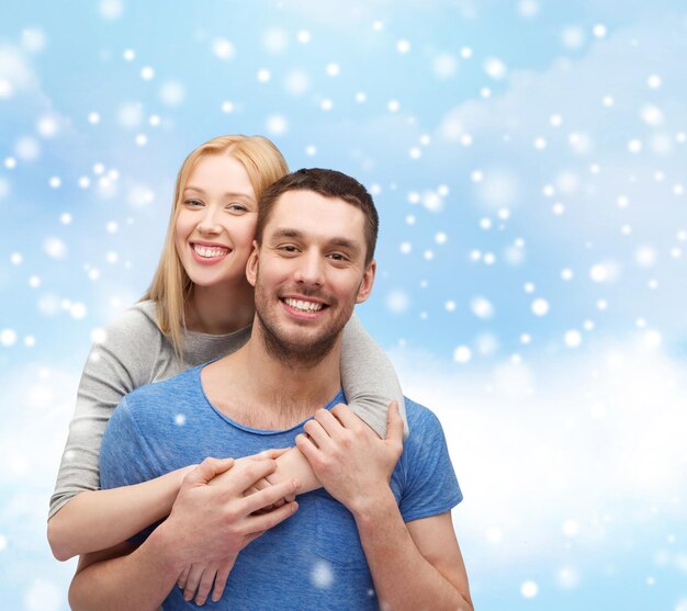 koncepcja miłości, ludzi i rodziny - uśmiechnięta para przytulająca się na tle błękitnego nieba, śniegu i chmur