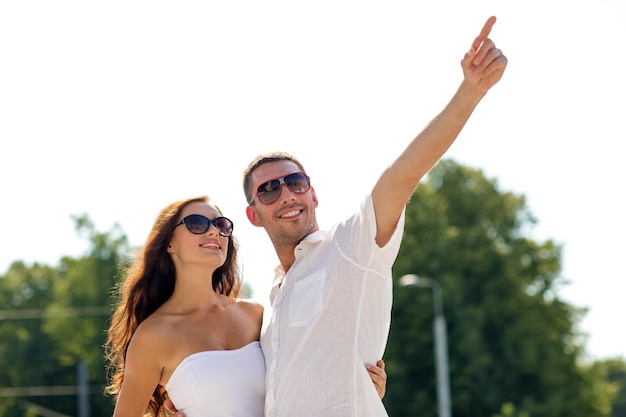 koncepcja miłości, podróży, turystyki, ludzi i przyjaźni - uśmiechnięta para w okularach przeciwsłonecznych, przytulająca się i wskazująca palcem w parku