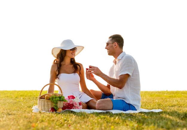 koncepcja miłości, randek, ludzi i świąt - uśmiechnięty młody człowiek pokazujący swojej dziewczynie małe czerwone pudełko prezentowe na pikniku