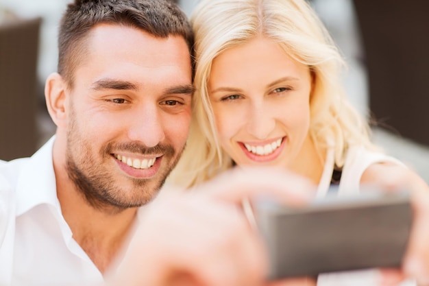koncepcja miłości, randki, technologii, ludzi i relacji - uśmiechnięta szczęśliwa para biorąca selfie ze smartfonem na zewnątrz