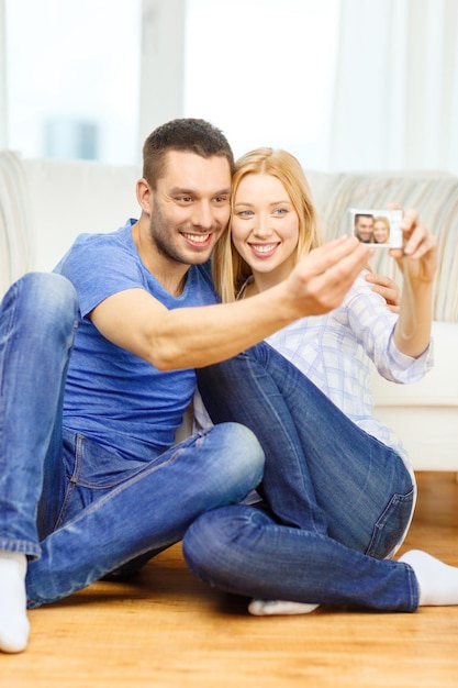 koncepcja miłości, rodziny, technologii i szczęścia - uśmiechnięta para robi sobie zdjęcie autoportretowe aparatem cyfrowym w domu