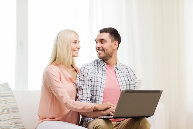koncepcja miłości, rodziny, technologii, internetu i szczęścia - uśmiechnięta szczęśliwa para z laptopem w domu
