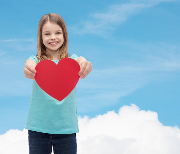 koncepcja miłości, szczęścia i ludzi - uśmiechnięta dziewczynka dająca czerwone serce