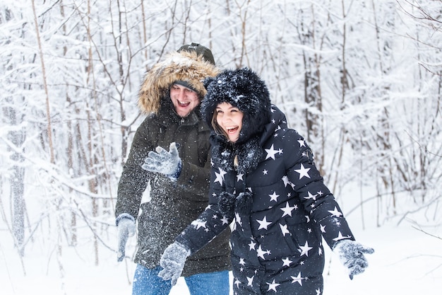Koncepcja miłości, związku, pory roku i przyjaźni - mężczyzna i kobieta bawią się i bawią się śniegiem w zimowym lesie
