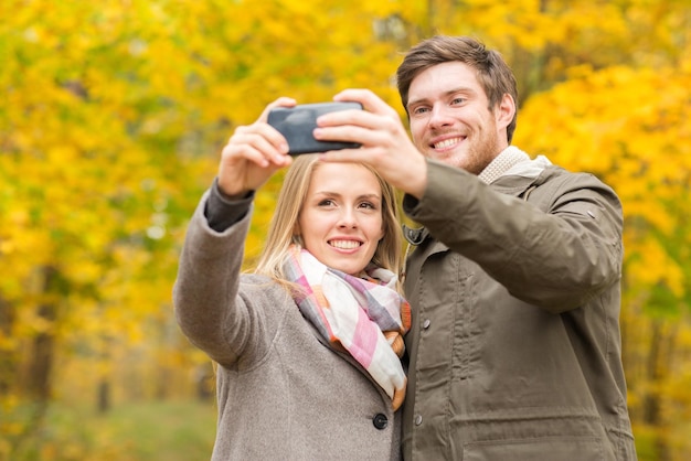 koncepcja miłości, związku, rodziny i ludzi - uśmiechnięta para przytulająca się i biorąca selfie w jesiennym parku