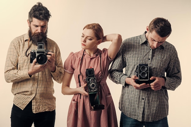 Koncepcja moda vintage. Mężczyźni i kobiety na zamyślonych twarzach na białym tle. Mężczyźni w kraciastych ubraniach, w stylu retro. Firma zapracowanych fotografów ze starymi aparatami, filmujących, pracujących.