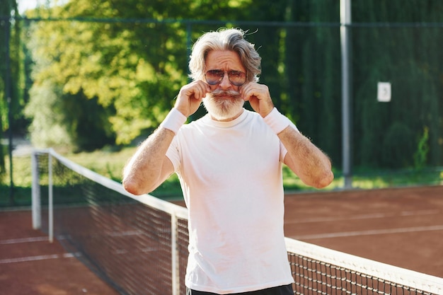 Koncepcja mody w okularach przeciwsłonecznych Starszy nowoczesny stylowy mężczyzna na zewnątrz na boisku sportowym w ciągu dnia