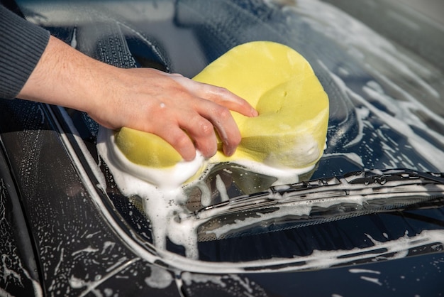 Koncepcja myjni samochodowej człowiek myje samochód mydłem i żółtą gąbką