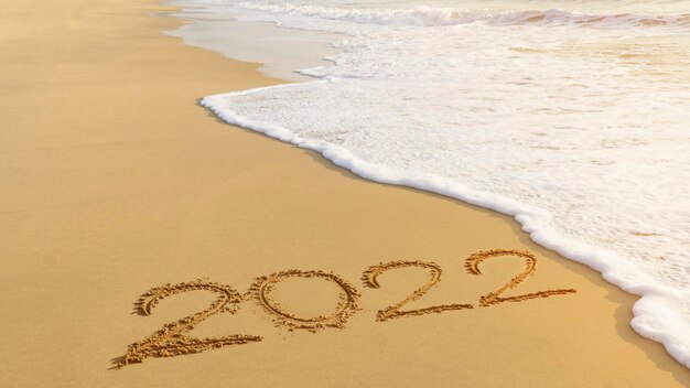 Koncepcja nadchodzącego szczęśliwego Nowego Roku 2022 napisana odręcznie na plaży