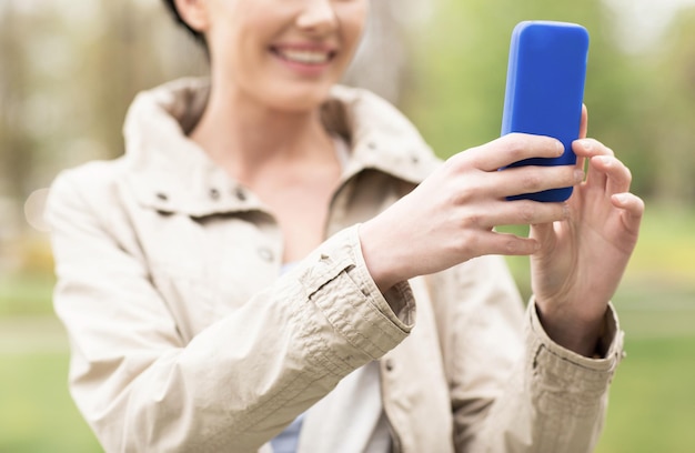 koncepcja napojów, wypoczynku, technologii i ludzi - uśmiechnięta kobieta robi zdjęcie lub selfie ze smartfonem w parku