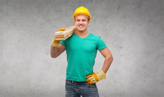 koncepcja naprawy, budowy i konserwacji - uśmiechnięty mężczyzna w kasku ochronnym niosący drewniane deski