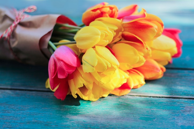 koncepcja nastroju wiosennego i nastroju romantycznego. bukiet różnokolorowych tulipanów leży na niebiesko-zielonym drewnianym stole. widok z góry.