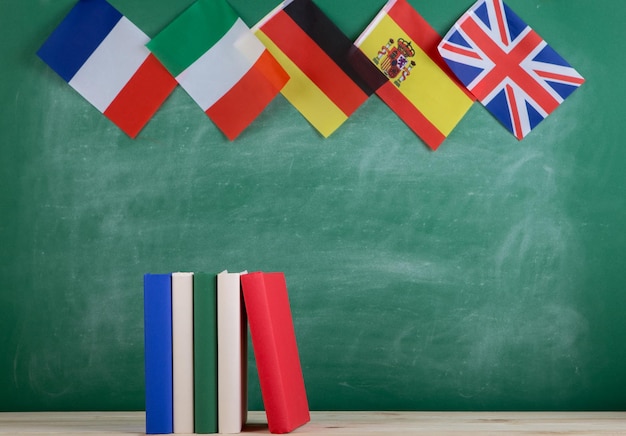 Koncepcja nauki języków - flagi Hiszpanii, Francji, Wielkiej Brytanii i innych krajów oraz książki na tle tablicy