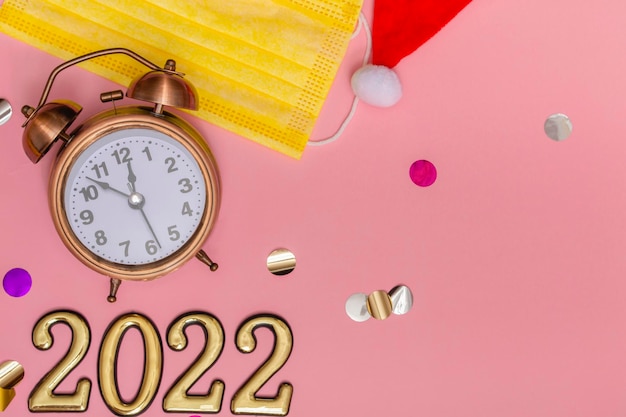 Koncepcja nowego roku na różowym tle budzik w żółtej masce medycznej złote liczby z bliska