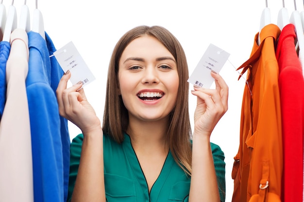 koncepcja odzieży, mody, sprzedaży, zakupów i ludzi - szczęśliwa kobieta pokazująca metki na ubraniach w domowej garderobie lub sklepie