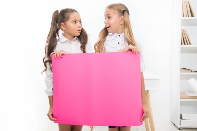 Koncepcja ogłoszenia szkolnego Zaskakujące wiadomości Dziewczęta trzymają baner z ogłoszeniem Dziewczęta trzymają papierowy baner do ogłoszenia Dzieci zaskoczone pustym papierem miejsca na kopię ogłoszenia szkolnego