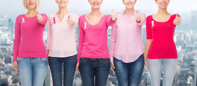 koncepcja opieki zdrowotnej, ludzi, gestów i medycyny - zbliżenie uśmiechniętych kobiet w pustych koszulach z różowymi wstążkami świadomości raka piersi na tle miasta