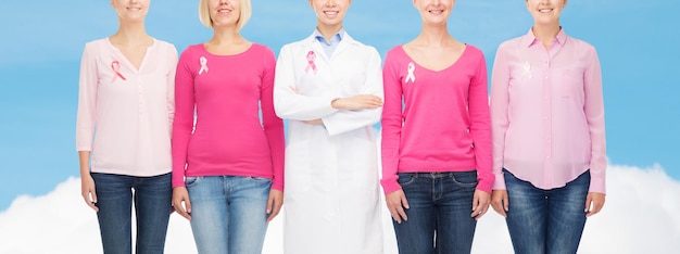 koncepcja opieki zdrowotnej, ludzi i medycyny - zbliżenie uśmiechniętych kobiet w pustych koszulach z różowymi wstążkami świadomości raka piersi na niebieskim niebie i białym tle chmury