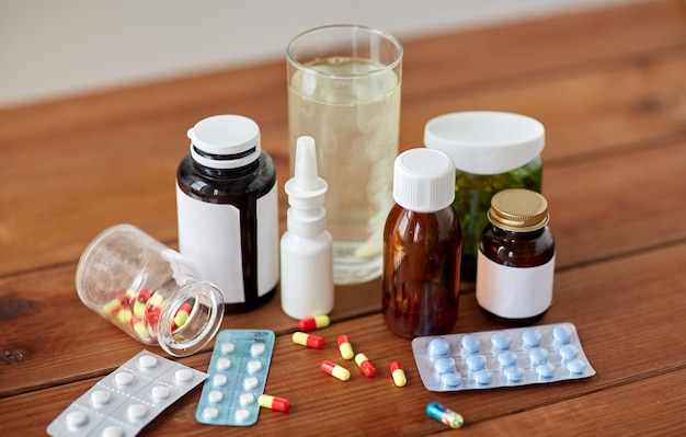 koncepcja opieki zdrowotnej, medycyny i leków - pigułki, aerozol do nosa, syrop przeciwgorączkowy i szkło na drewnianym stole