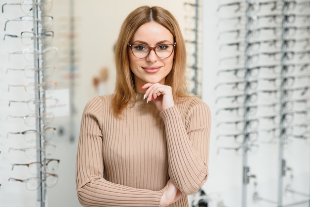 Koncepcja Opieki Zdrowotnej, Wzroku I Wzroku - Szczęśliwa Kobieta Wybierając Okulary W Sklepie Optycznym. Portret Piękna Młoda Kobieta Próbuje Nowych Okularów W Sklepie Optyka