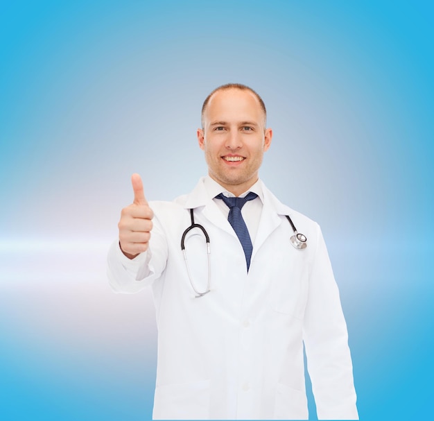koncepcja opieki zdrowotnej, zawodu, gestów i medycyny - uśmiechnięty mężczyzna lekarz ze stetoskopem pokazujący kciuki w górę na niebieskim tle