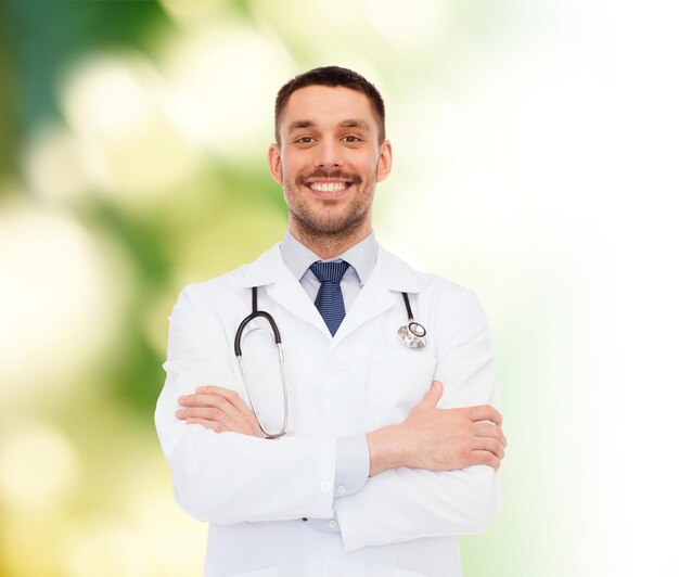 koncepcja opieki zdrowotnej, zawodu i medycyny - uśmiechnięty mężczyzna lekarz ze stetoskopem w białym fartuchu na białym tle