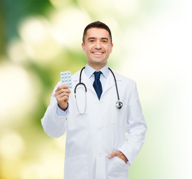 koncepcja opieki zdrowotnej, zawodu, ludzi i medycyny - uśmiechnięty mężczyzna lekarz w białym fartuchu z tabletami na zielonym tle