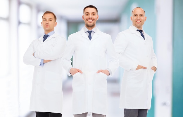 koncepcja opieki zdrowotnej, zawodu, pracy zespołowej i medycyny - uśmiechnięci lekarze płci męskiej w białych fartuchach na tle korytarza szpitalnego