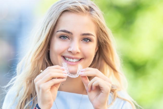 Koncepcja ortodoncji Invisalign - młoda atrakcyjna kobieta trzyma - za pomocą niewidocznych szelek lub trenera.