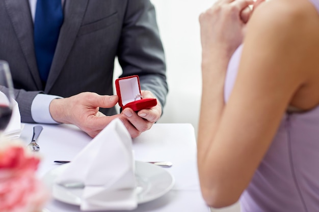 Zdjęcie koncepcja para, miłość, zaręczyny i wakacje - zbliżenie podekscytowanej młodej kobiety i chłopaka dającego pierścionek w restauracji
