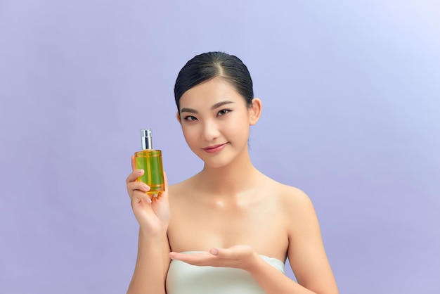 Koncepcja pielęgnacji ciała i pielęgnacji skóry Uśmiechnięta dorosła azjatycka kobieta pokazująca butelkę z dozownikiem z mydłem pod prysznic lub olejkiem do pielęgnacji ciała na fioletowym tle