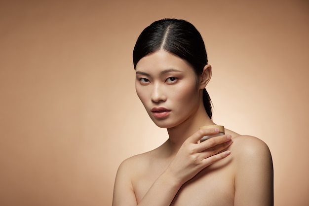 Koncepcja pielęgnacji skóry - urocza młoda azjatycka kobieta trzyma butelkę w sprayuand balsam z doskonałą kompozycją zdjęć makijażu brunetki