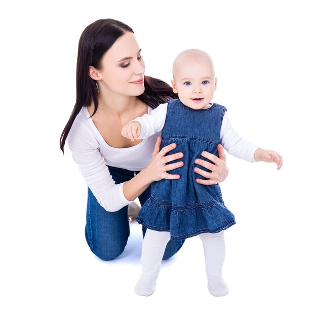 Koncepcja pierwszego kroku - szczęśliwa młoda matka bawi się z córeczką na białym tle