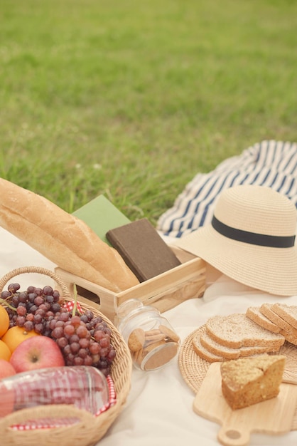 Koncepcja piknikowa posiłek piknikowy na białym obrusie składający się z koszyka z bidonem, jabłek, pomarańczy i winogron, bochenka chleba, słoika ciasteczek i kromek chleba.