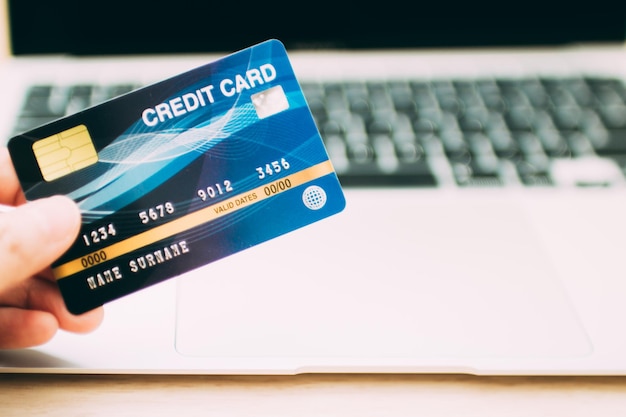 Koncepcja płatności online. Ręka trzyma kartę kredytową i za pomocą laptopa do zakupów online.