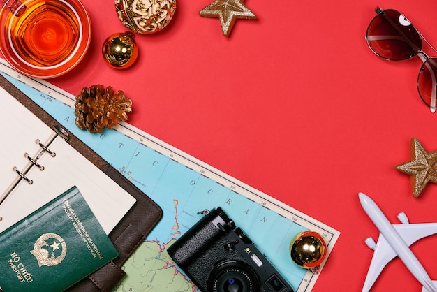 Koncepcja podróży HOLIDAY - paszport, aparat fotograficzny, czapka, samolot, ozdoby świąteczne na czerwonym tle