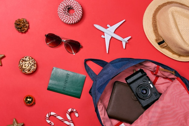 Koncepcja podróży HOLIDAY - paszport, aparat fotograficzny, czapka, samolot, ozdoby świąteczne na czerwonym tle