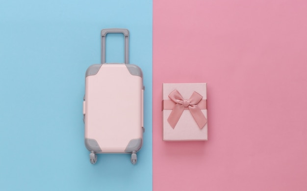 Koncepcja podróży. Mini walizka podróżna z tworzywa sztucznego i pudełka na prezenty na różowym niebieskim tle pastelowych. Minimalistyczny styl. Widok z góry, układ płaski