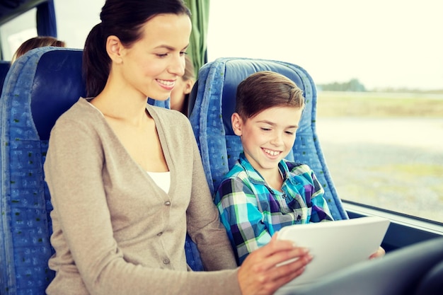 koncepcja podróży, turystyki, rodziny, technologii i ludzi - szczęśliwa matka i syn z komputerem typu tablet PC siedzącym w autobusie podróżnym