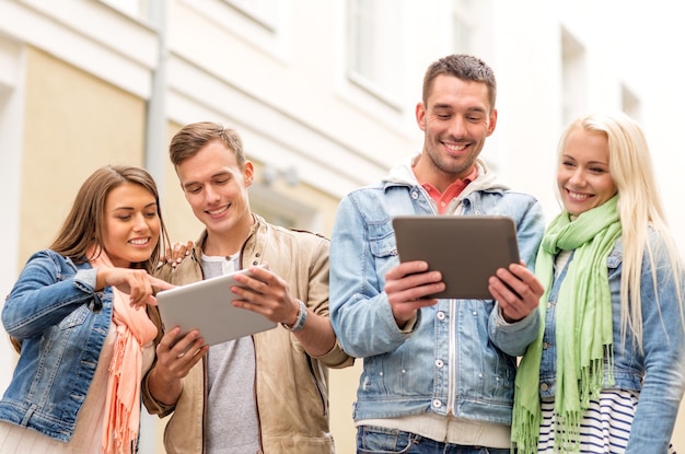 koncepcja podróży, wakacji, technologii i przyjaźni - grupa uśmiechniętych przyjaciół z komputerami typu tablet w mieście