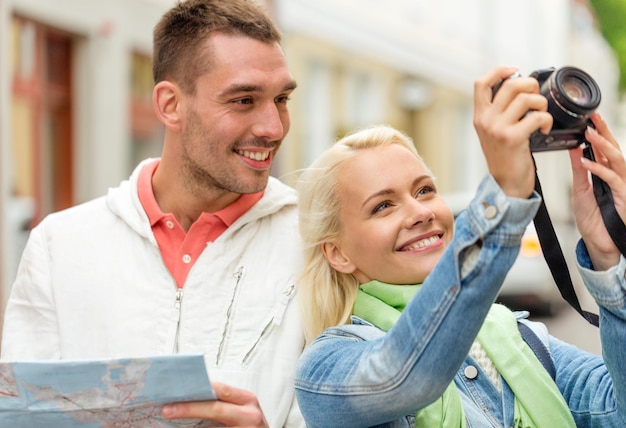 Koncepcja Podróży, Wakacji, Technologii I Przyjaźni - Uśmiechnięta Para Z Mapą I Aparatem Fotograficznym Eksplorująca Miasto