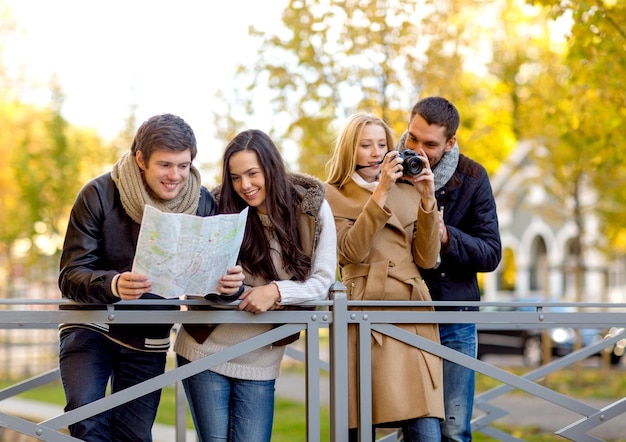 koncepcja podróży, wakacji, technologii, turystyki i przyjaźni - grupa uśmiechniętych przyjaciół z cyfrowym aparatem fotograficznym i mapą w parku miejskim