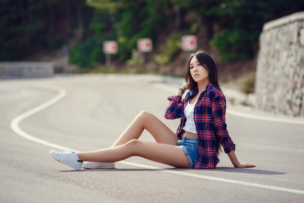 Koncepcja podróży wolnościowej letni weekend hipsterska dziewczyna wanderlust chodząca asfaltową drogą na dzikich ziemiach Piękna młoda dziewczyna o wyglądzie południowej Azji