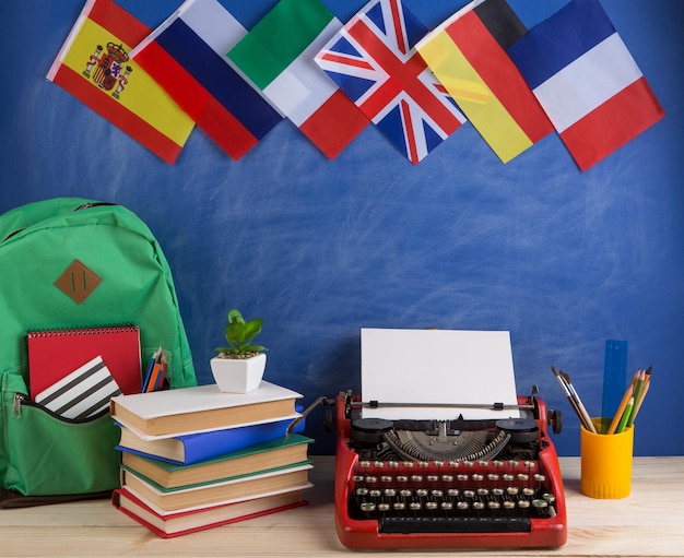 Koncepcja polityczna, wiadomości i edukacja - czerwona maszyna do pisania, flagi Hiszpanii, Francji, Wielkiej Brytanii i innych krajów, plecak, książki, artykuły papiernicze na tle tablicy