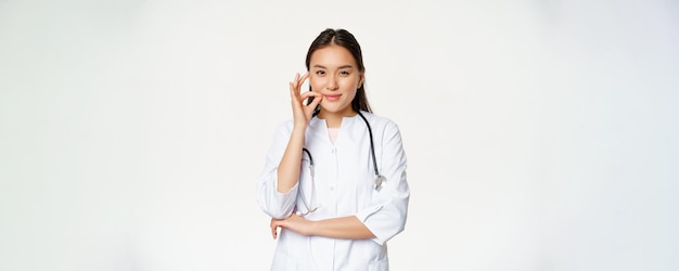 Koncepcja poufności medycznej tabu Młoda azjatycka lekarka pokazująca usta cisza tabu lub gest zip obietnica nie mów stojąc na białym tle